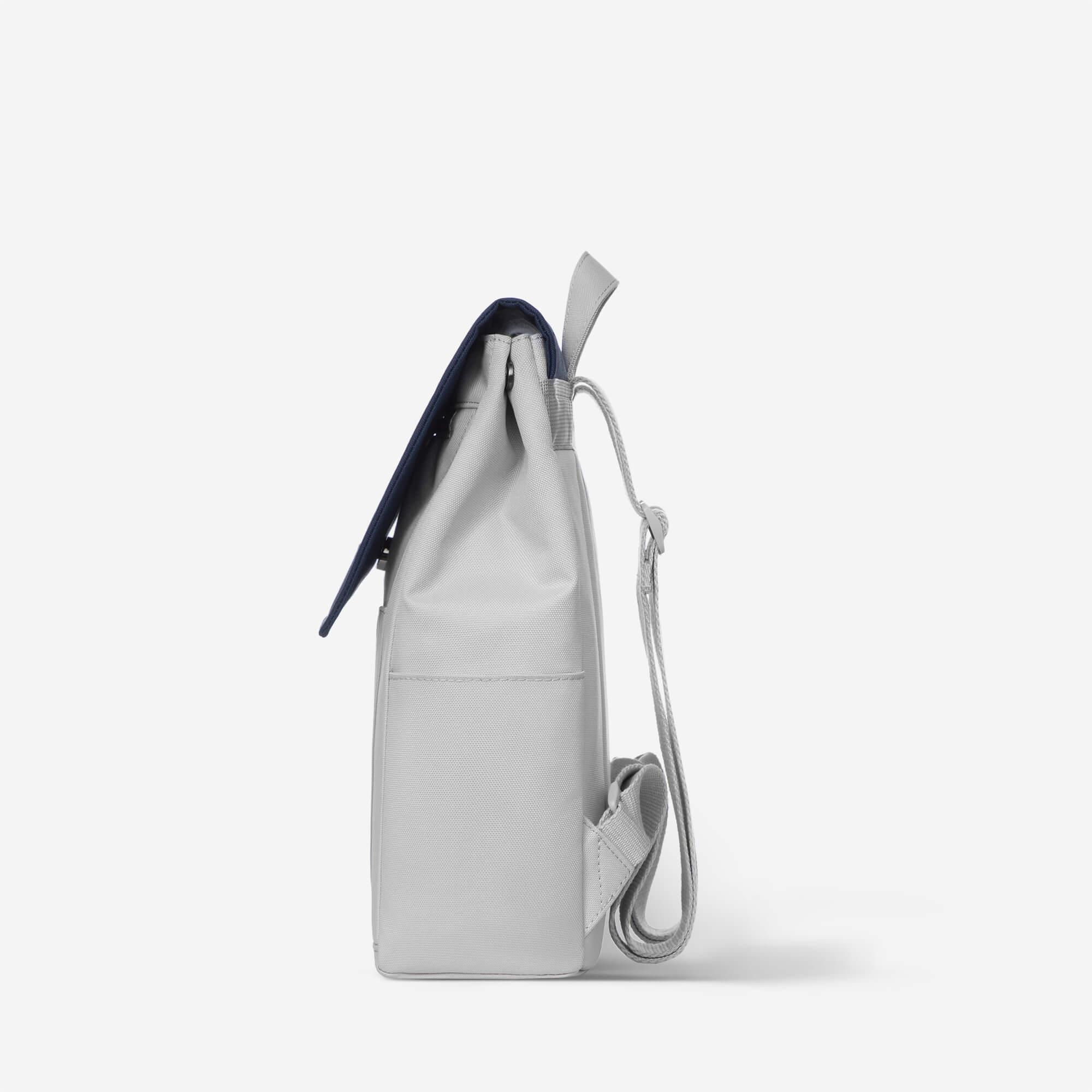 Light gray drawstring backpack with navy blue flap and adjustable shoulder strap, minimalist design