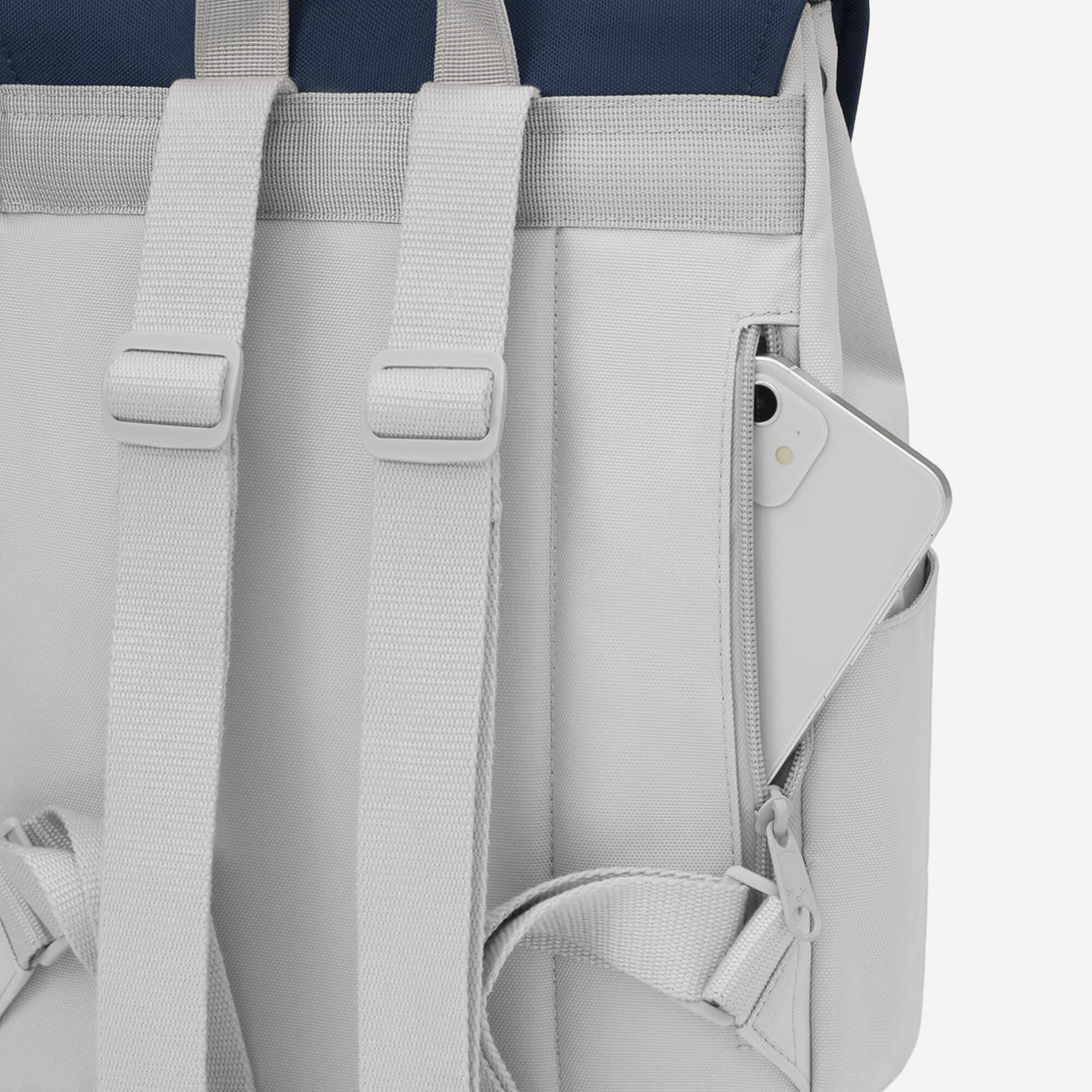 Gray backpack with side pocket holding phone, adjustable straps, and navy top panel