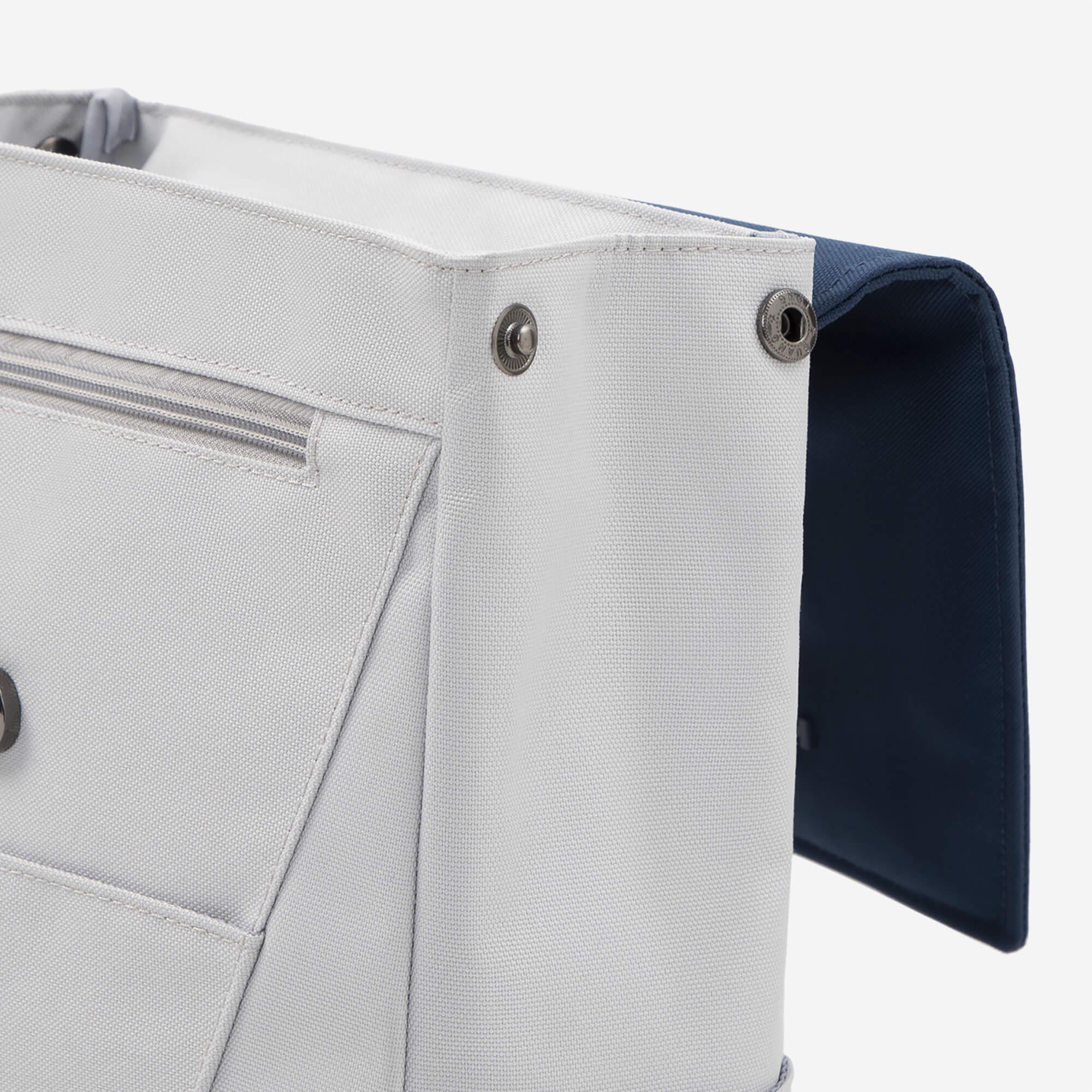 Light gray canvas tote bag with navy interior, zipper pocket, and metal snap buttons for secure closure.
