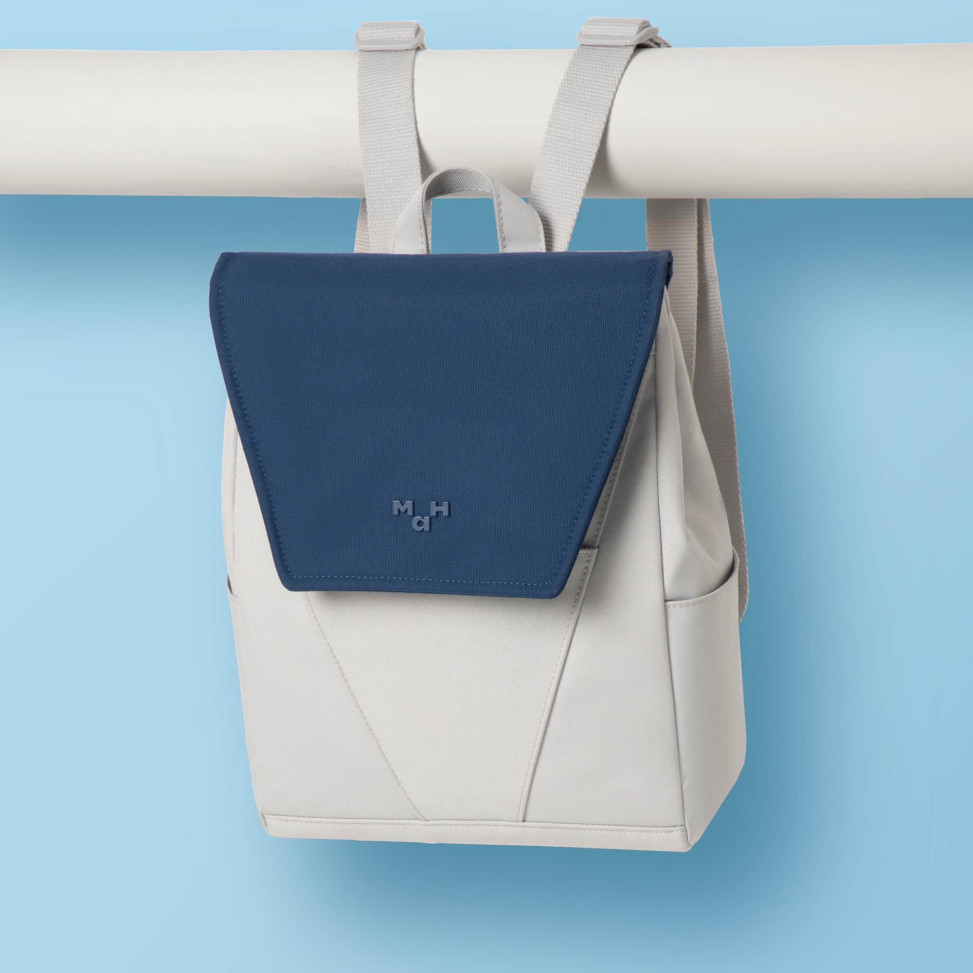 Navy and beige minimalist backpack with geometric flap, hanging on white rail against blue background