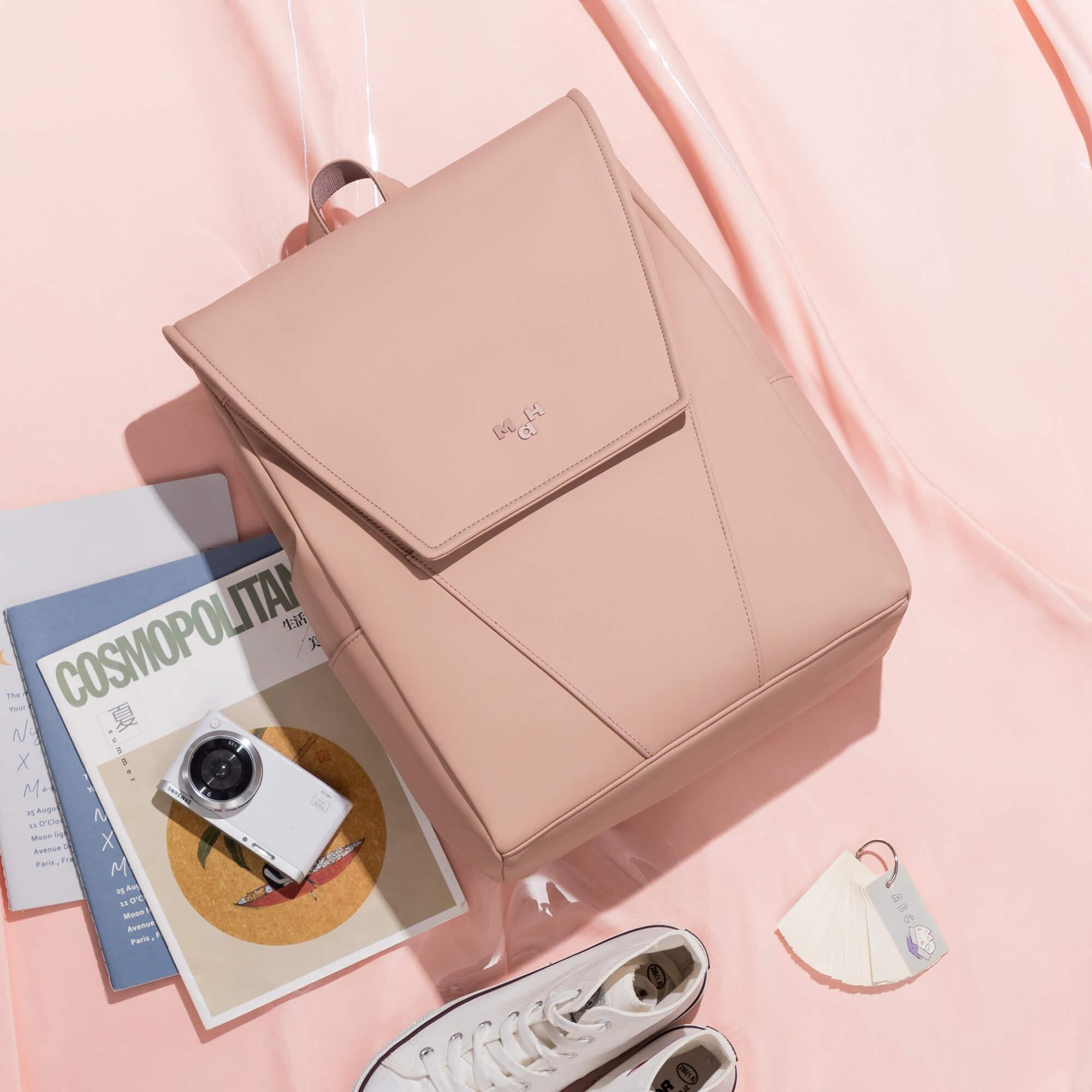 Pink minimalist backpack with sleek design, styled with magazines, camera, and white sneakers on soft pink background