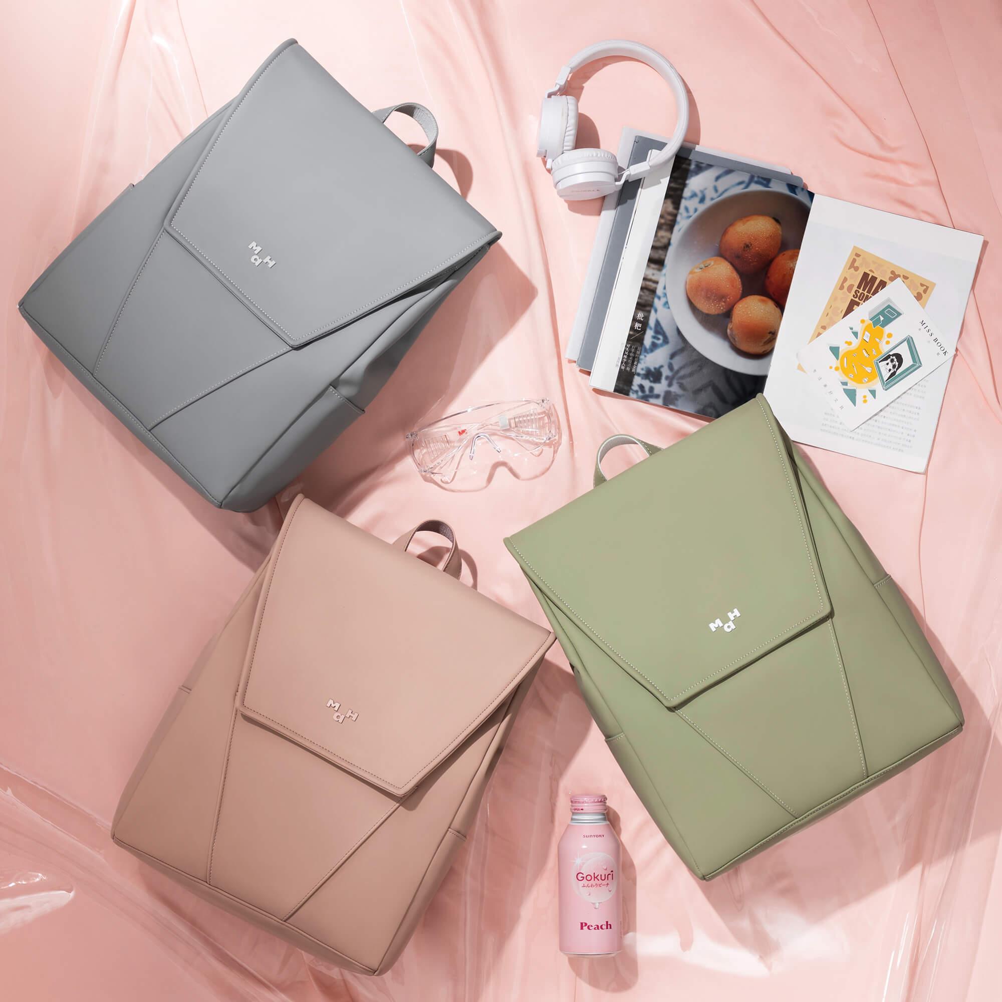 Stylish gray, blush, and olive backpacks with modern design, paired with headphones, magazines, and a peach drink on pink backdrop.