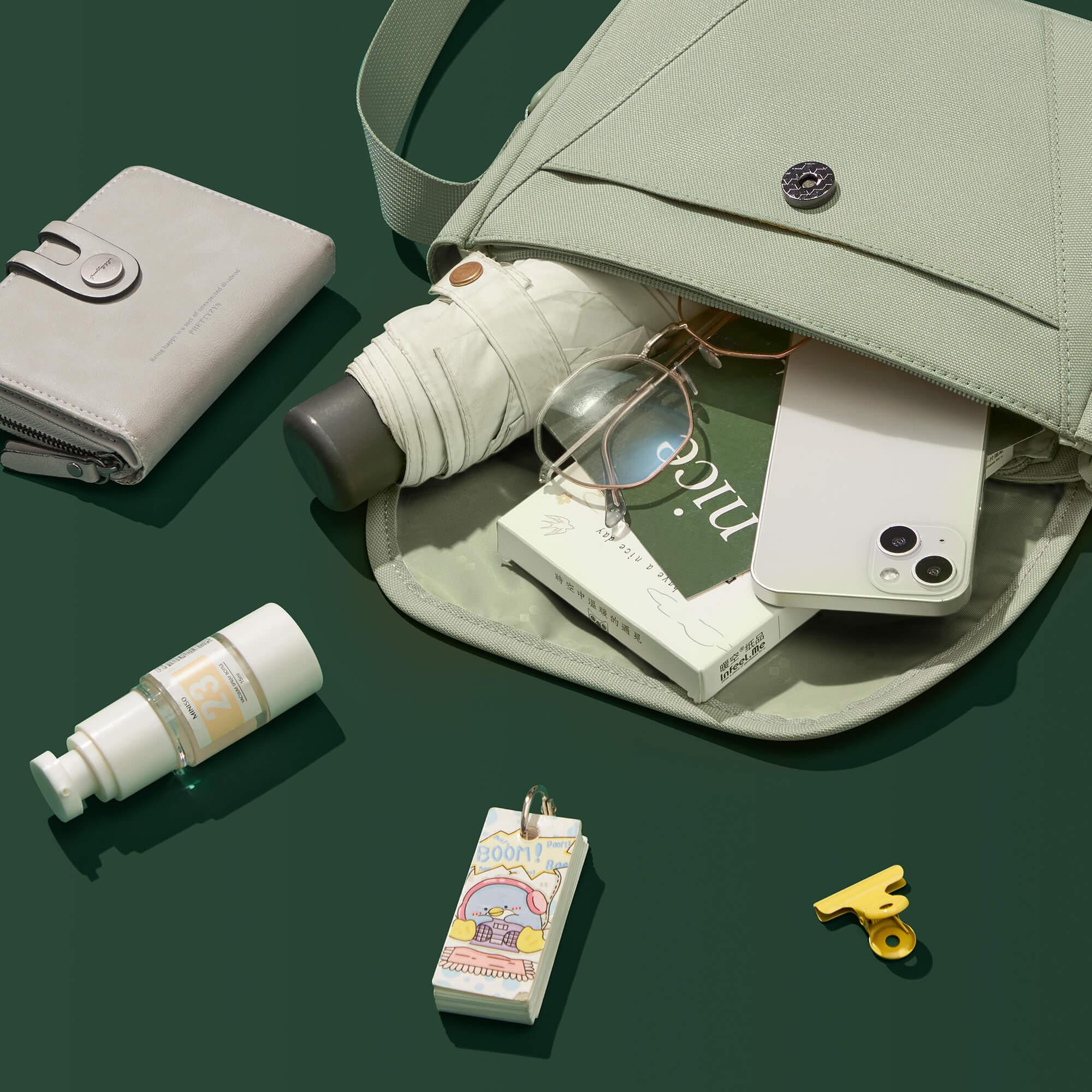 Light green canvas bag with phone, glasses, umbrella, wallet, and accessories on green background