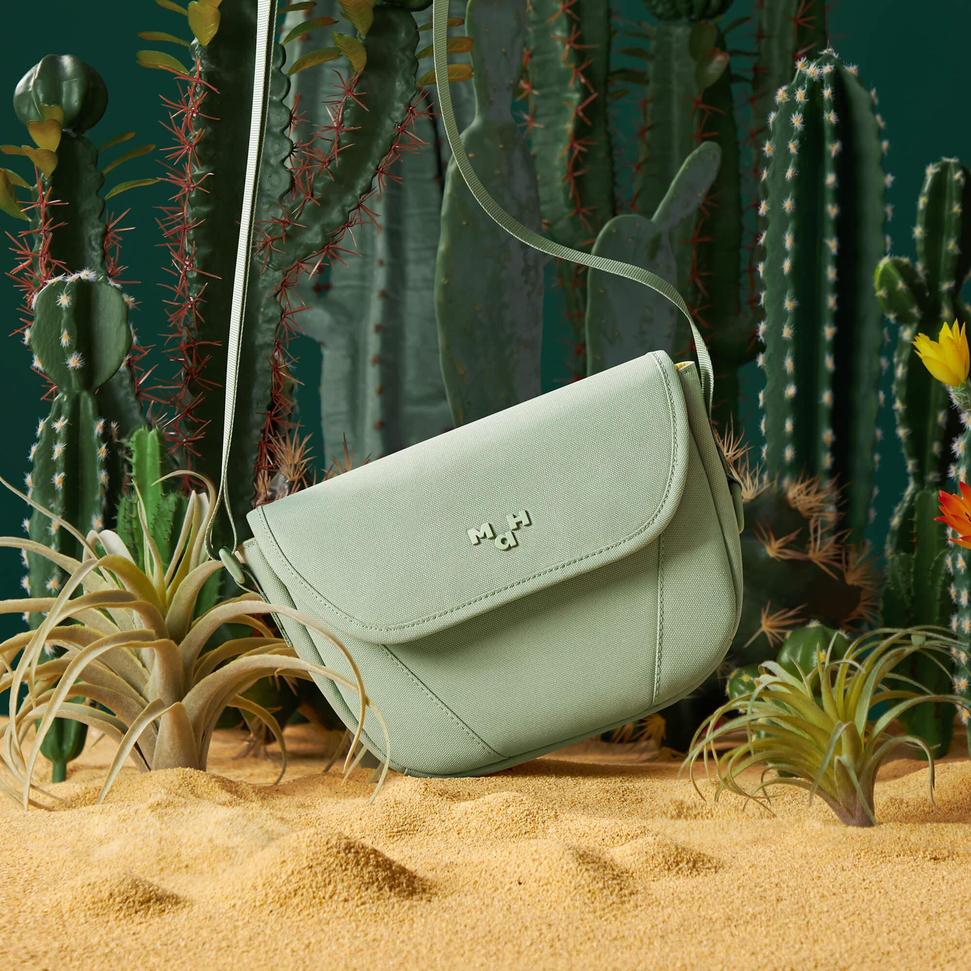 Mint green crossbody bag with adjustable strap, styled in desert sand with cacti and succulents.