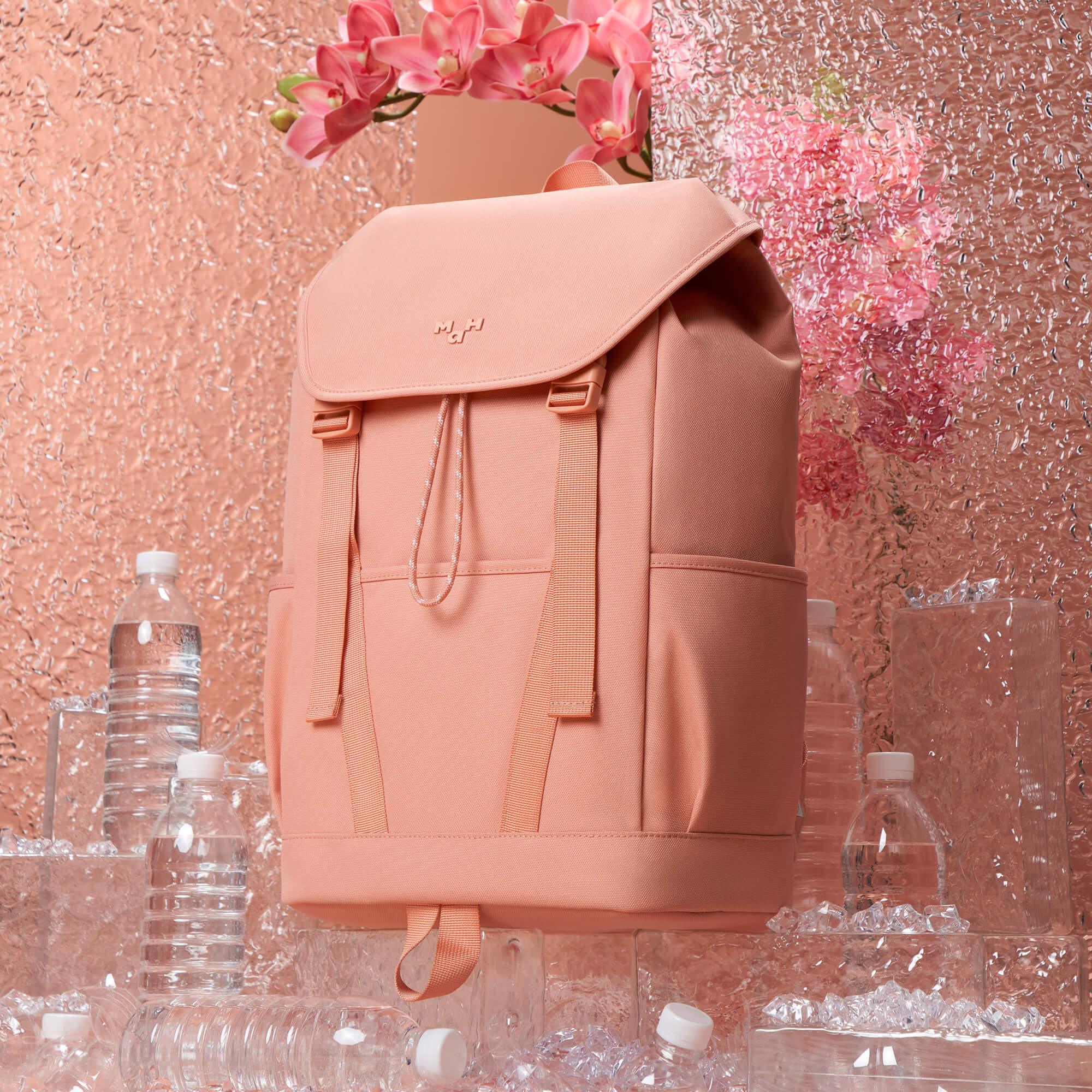 Soft pink backpack with drawstring closure, water bottles, and pink orchids on textured backdrop