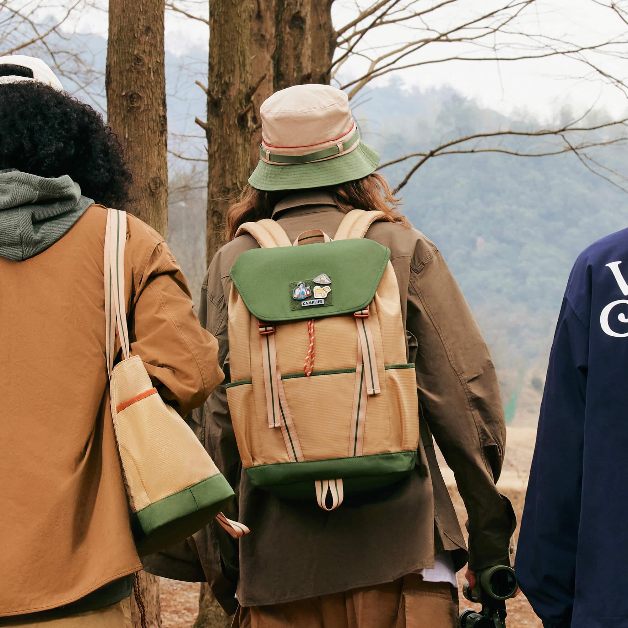 Green and beige backpack with patches, worn outdoors in forest setting, ideal for hiking and travel