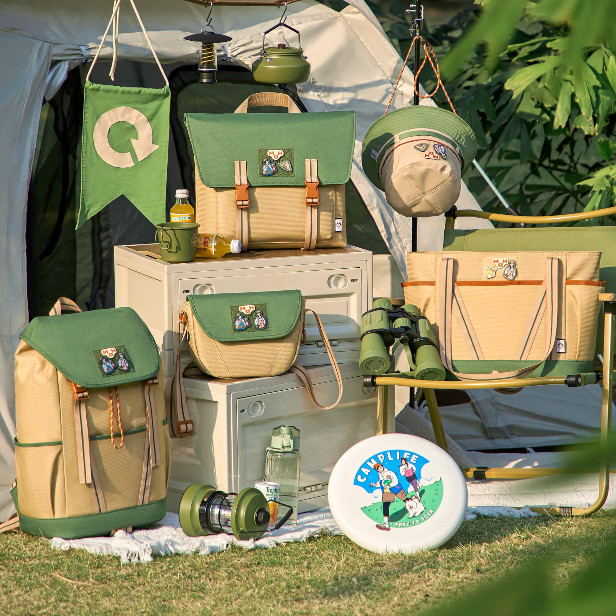 Green and beige camping gear set with backpacks, tote bags, hat, and accessories at a tent site