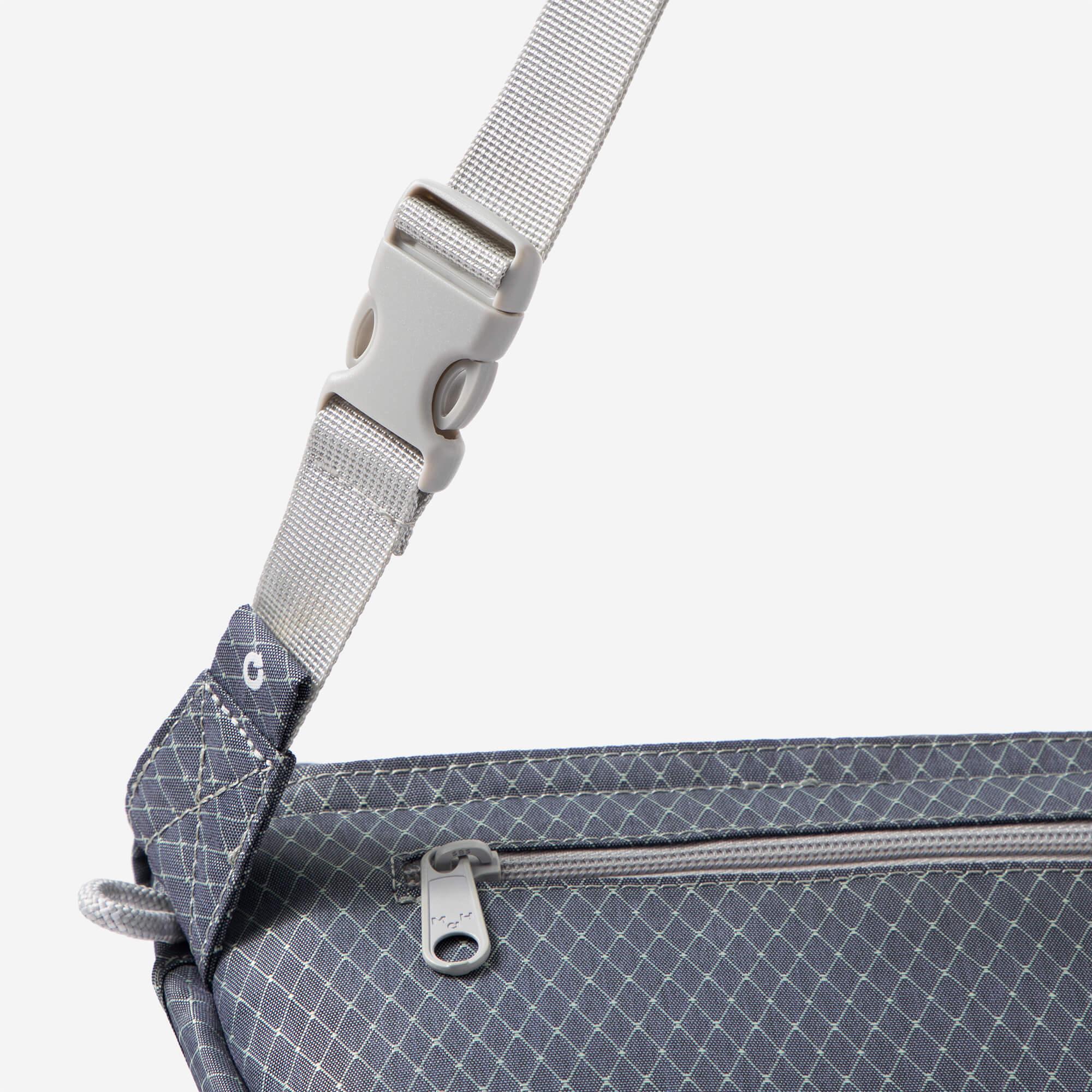 Adjustable strap with buckle on patterned crossbody bag, featuring zipper pocket and durable fabric.