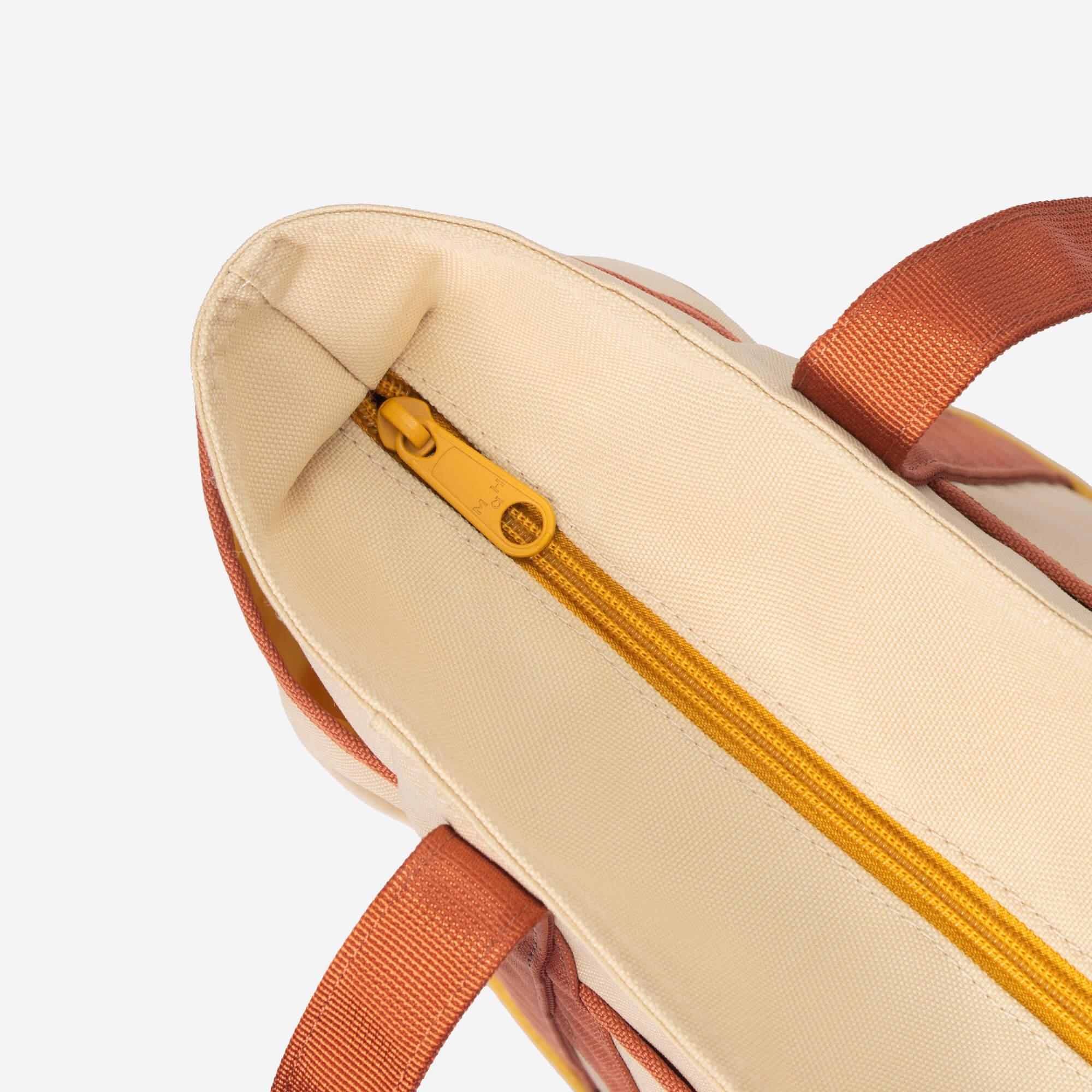 Cream canvas tote bag with mustard zipper and rust straps, lifestyle accessory detail