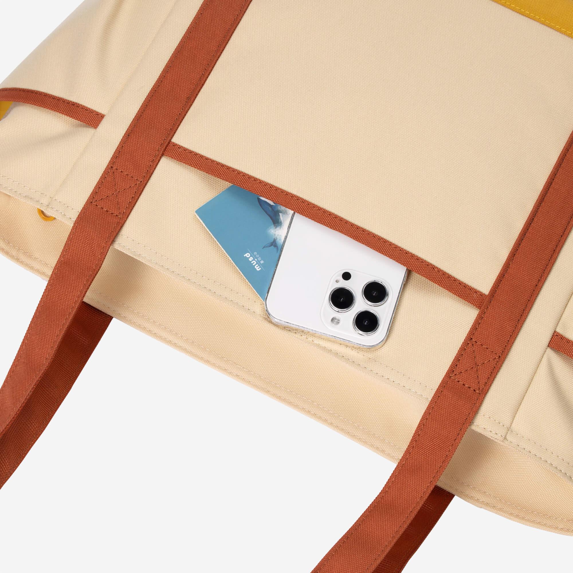 Beige canvas tote bag with brown straps holding a white smartphone and card, showcasing practical everyday carry design.
