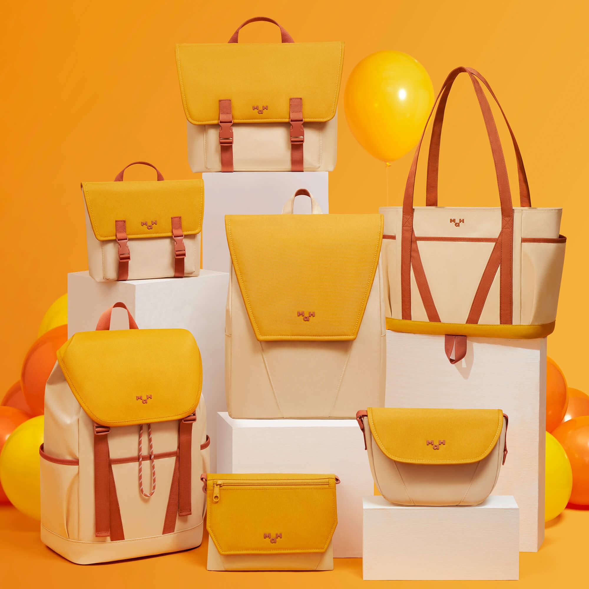 Stylish yellow and cream backpacks, totes, and accessories displayed on white blocks with balloons against orange background