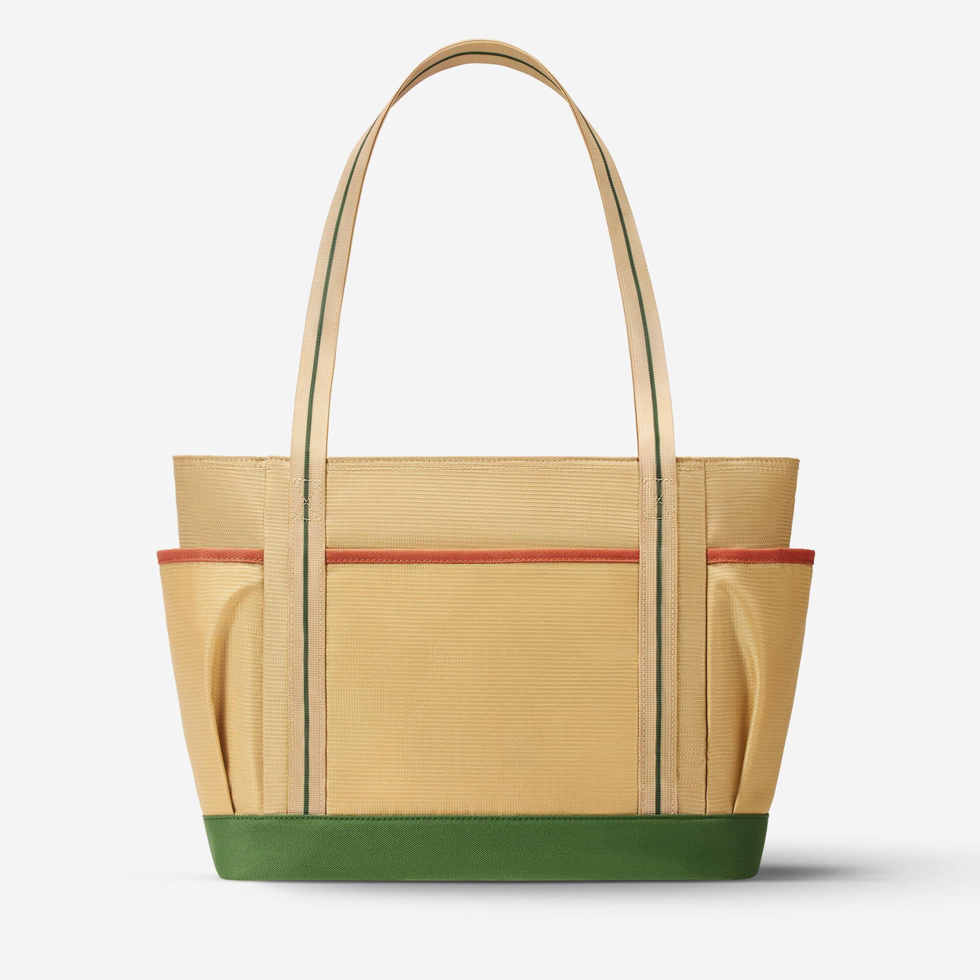 Beige tote bag with green base and orange trim, featuring striped handles and side pockets for everyday carry.