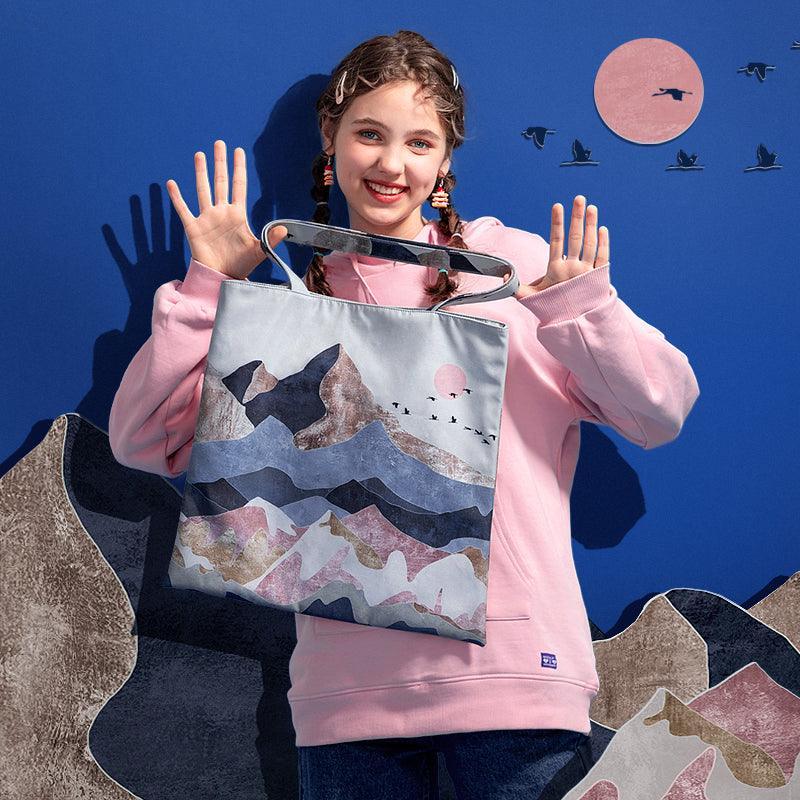 Girl holding mountain-print tote bag with birds and sunset design, stylish everyday accessory